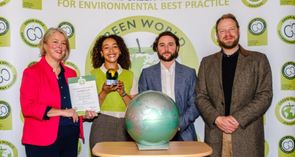 Trustgreen team stand beside event host holding their Green World Award trophy and certificate, a large globe on a podium sits in front of them